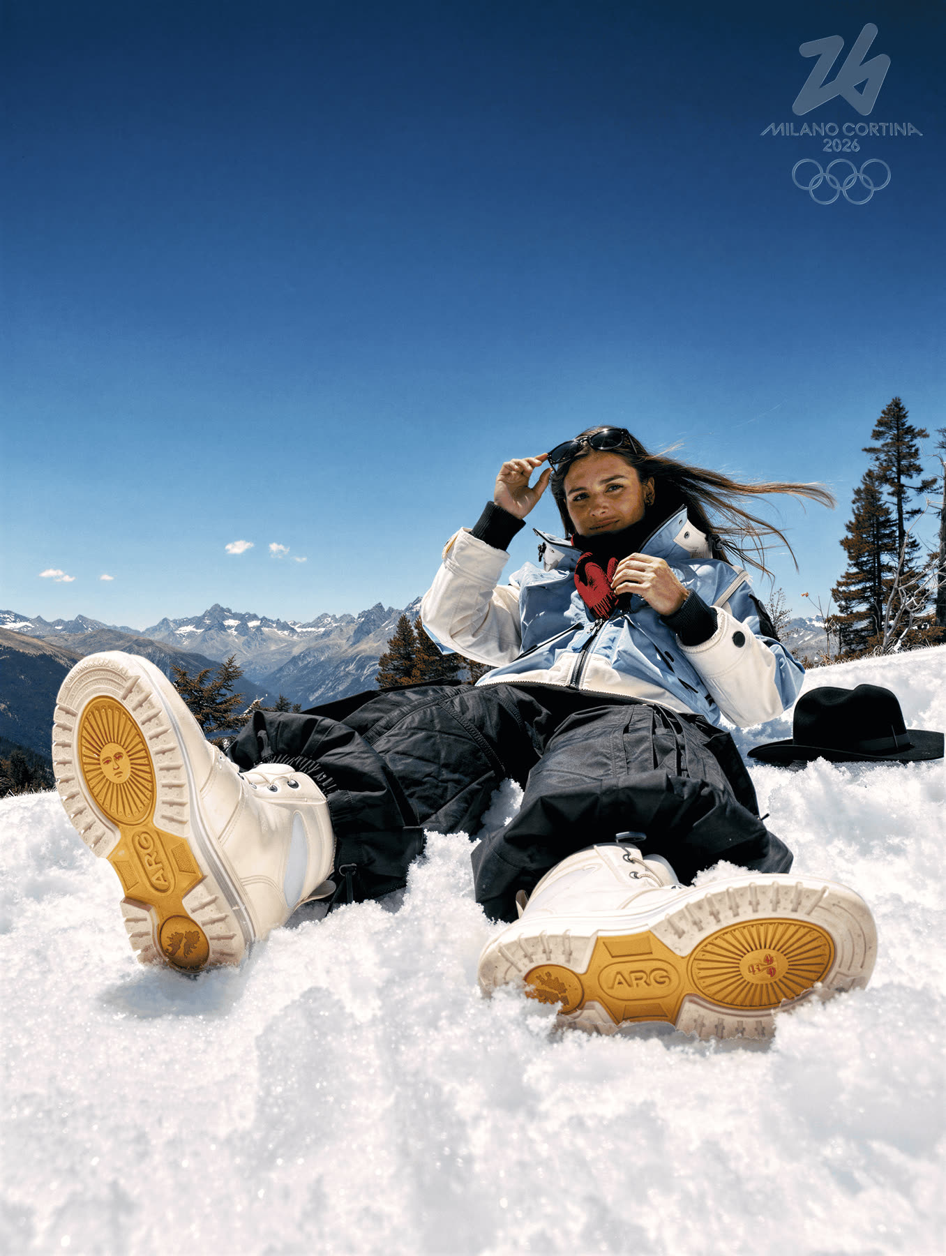 Athlete lying back in the snow, boots toward camera.